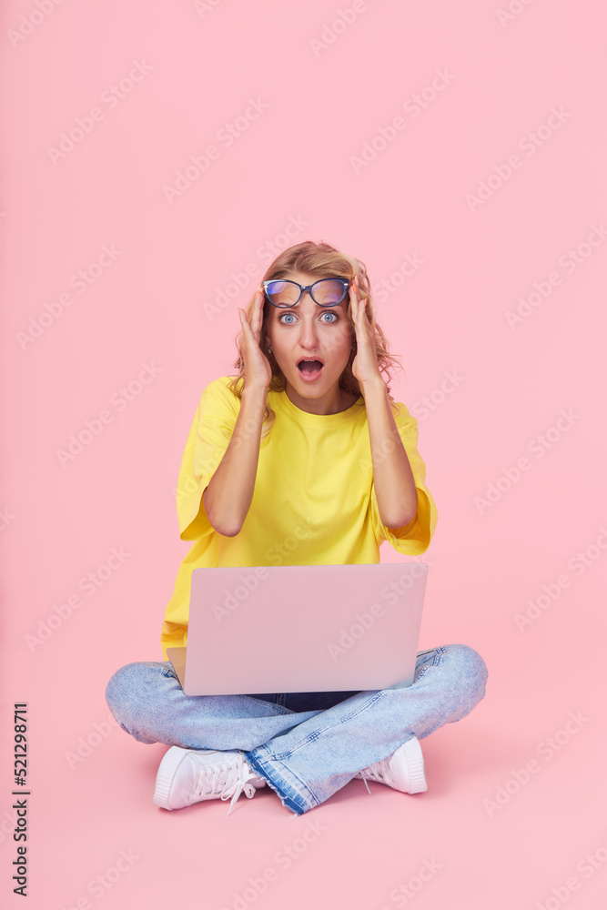 Full leight Portrait of a young surprised girl in casual clothes with a laptop in her hands on a pink background. The concept of learning and job search online Full leight Portrait of a young surprised girl in casual clothes with a laptop in her hands on a pink background. The concept of learning and job search online