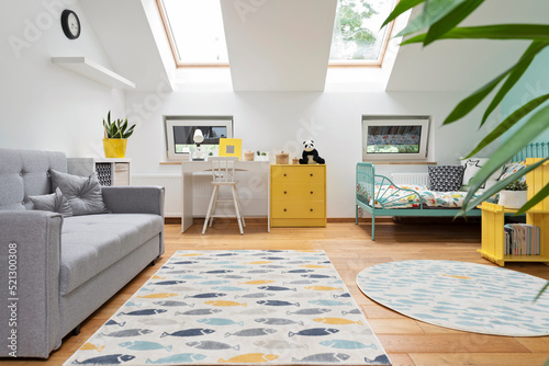 Child room in modern design in the attic with window. Bed, desk and sofa with yellow decor in cozy interior for children. Carpet on wooden floor.  Scandinavian style. photo