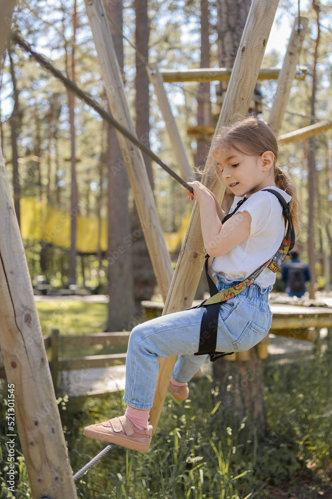 Little child girl climbing in adventure park. Summer camp.