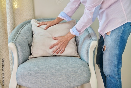 A woman decorating blue armchair with velvet beige cushion