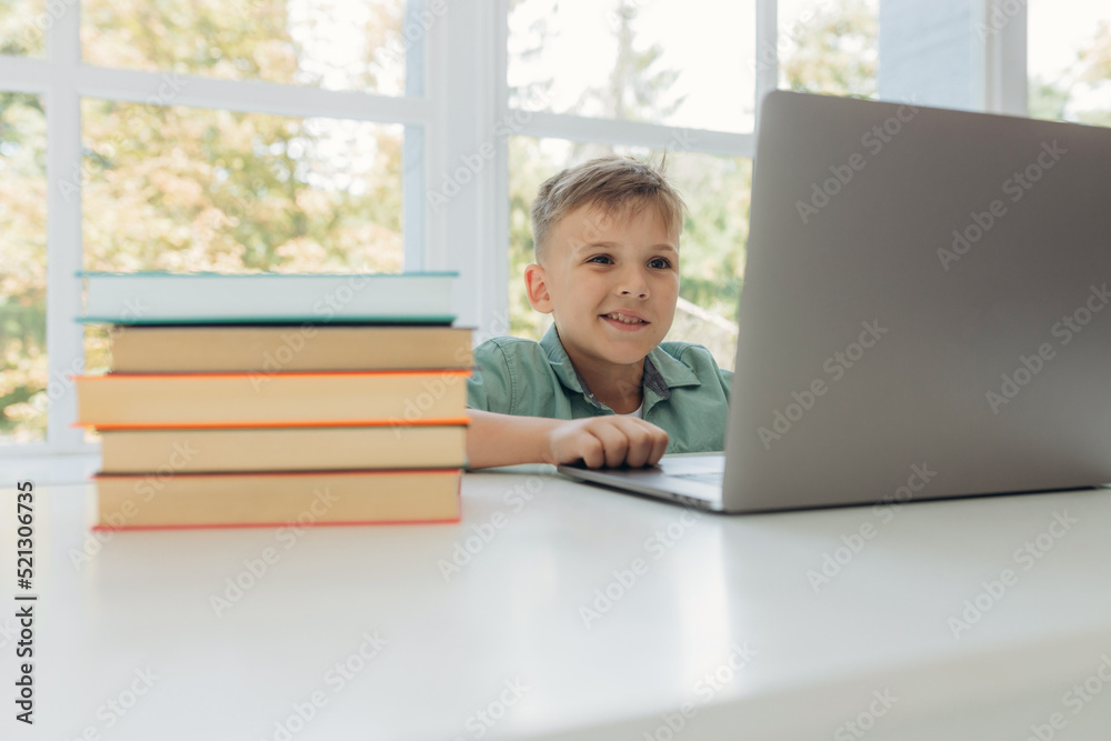 Distance learning online education. Schoolboy boy studies at home with laptop and does school homework. Training books and notebooks on table Distance learning online education. Schoolboy boy studies at home with laptop and does school homework. Training books and notebooks on table