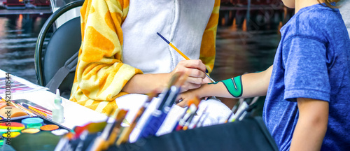Young girl artist draws a dragon on child's hand. Process of drawing on skin, close-up, banner.