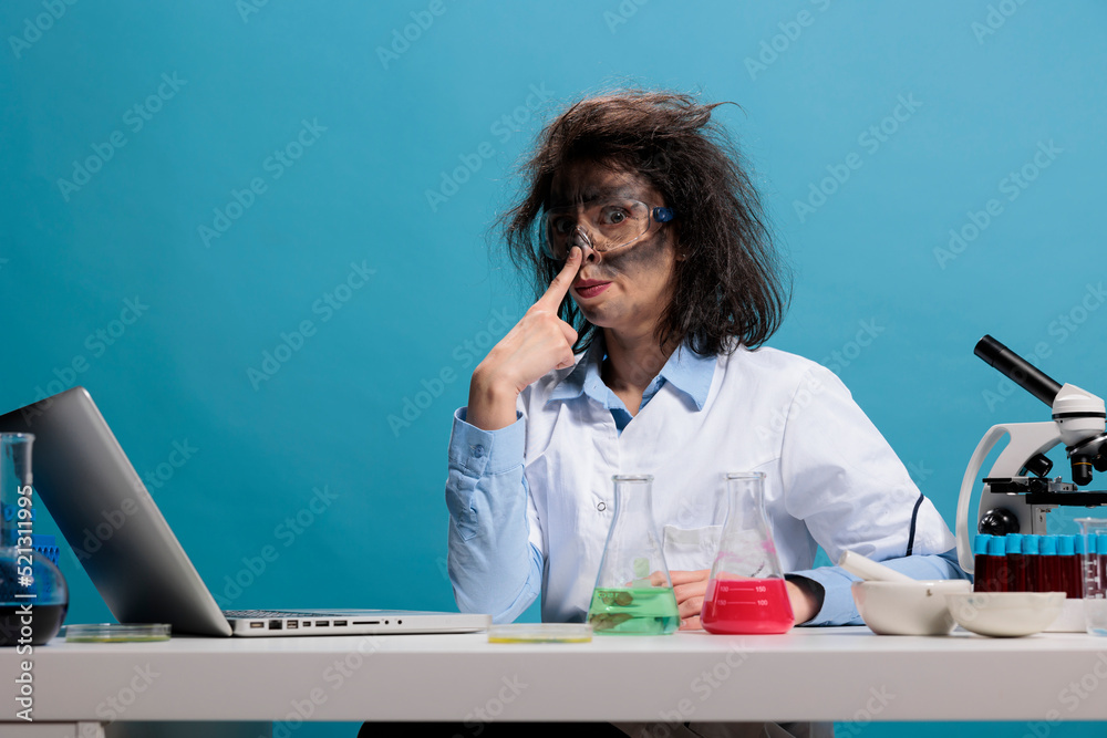 Portrait of crazy amusing chemist acting funny and having dirty face and  messy hair while sitting