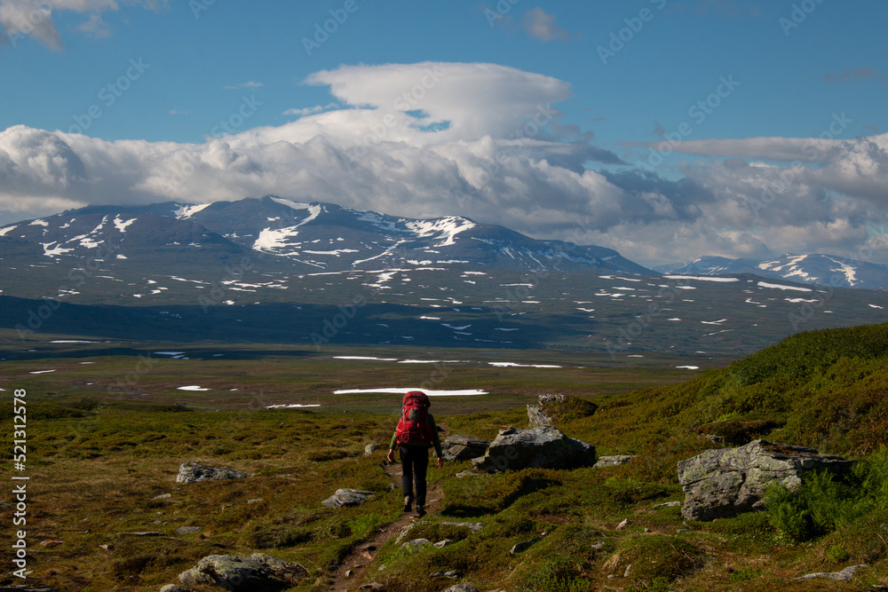 A hiker with a huge backpack on a trail between the Swedish Blahammaren and Norwegian Storerikvollen Mountain stations, Jamtland, Sweden