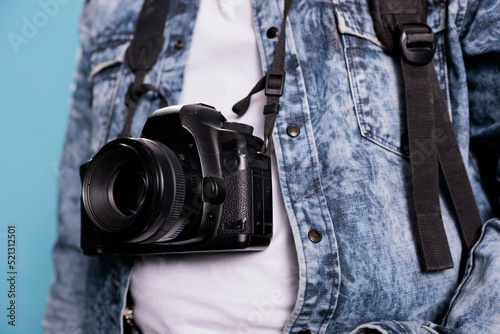 Close up shot of photographer wearing denim jacket and having modern photo device. Photography enthusiast having professional DSLR camera while standing on blue background. Studio shot