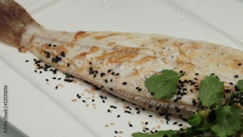 Food display of a plate of Sole meuniere with greens and sesame seeds spinning on white surface photo