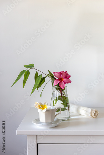 Plumberia rumba in a coffe cup, eucalyptus branch in a vase and cup of coffee on a white table against a wall with two frames. Ready layout. Vertical frame. Space for text