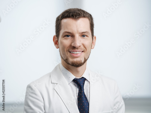 Closeup portrait of smiling male dentist in white lab coat looking at camera © Anton Zabielskyi