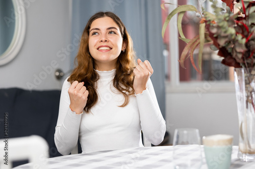 Portrait of young successful woman sitting at table in apartment and clenching her fists. photo