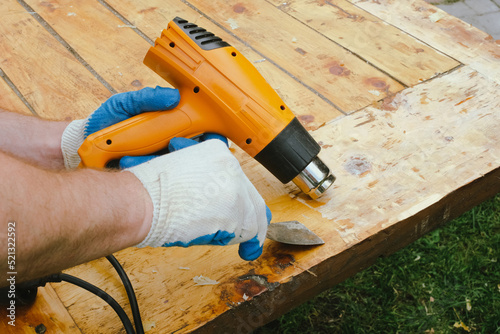 Man removing old varnish from wood using scraper and heat gun. photo