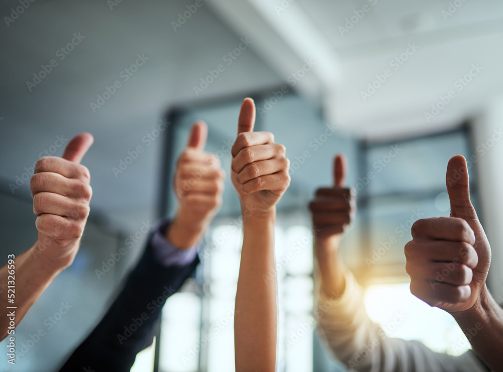 Closeup of business people showing thumbs up hand sign in a modern office. Diverse group of