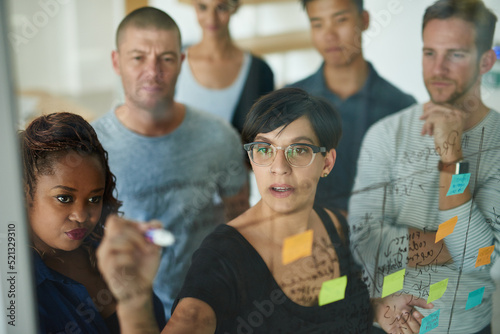Smart, thinking business people planning and writing ideas on a transparent board while working together on a group project. Busy and organized workers creating a schedule and plans with sticky notes