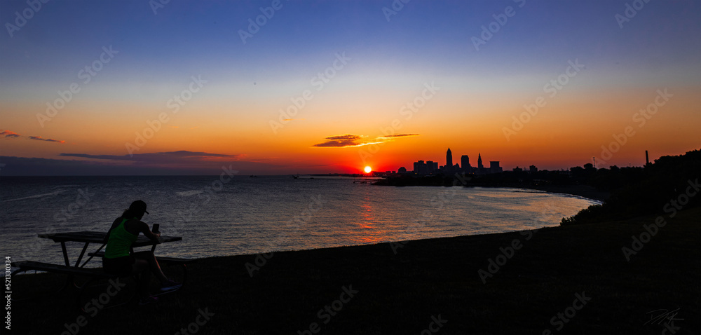 Obraz premium Woman catches sunrise over Lake Erie and Downtown Cleveland