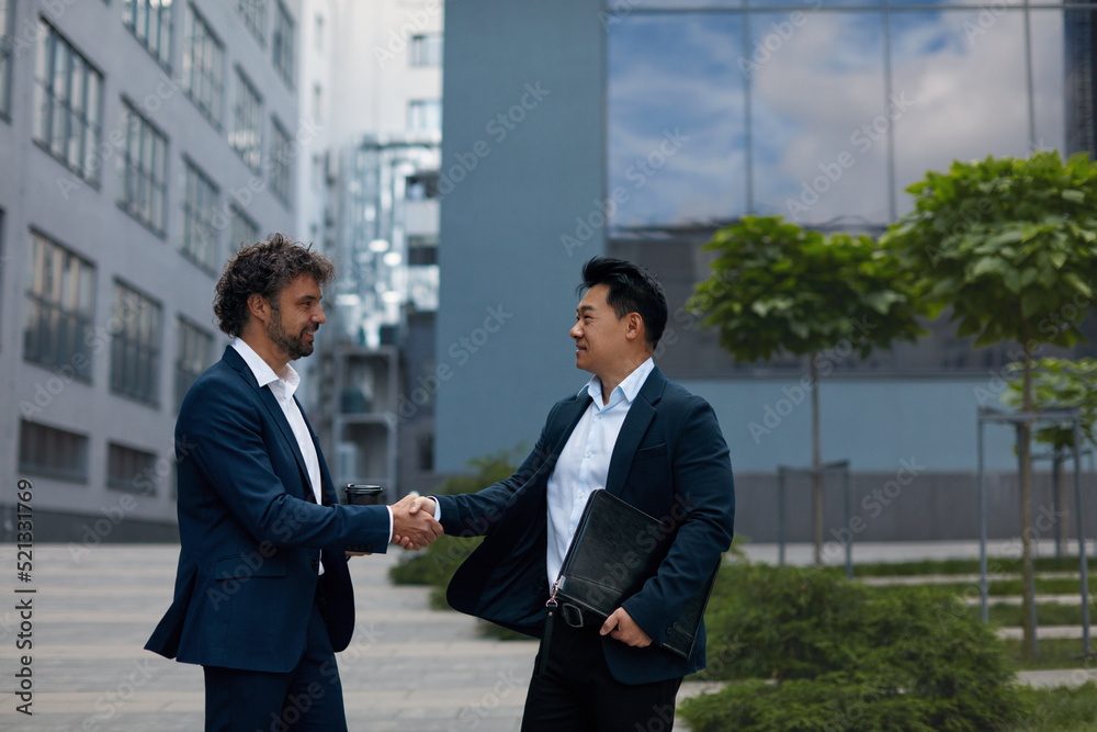 Lucky Multicultural Partners Shaking Hands on Meeting in City. Professional Multiethnic Businesspeople near Office Building, side view. Teamwork Concept Lucky Multicultural Partners Shaking Hands on Meeting in City. Professional Multiethnic Businesspeople near Office Building, side view. Teamwork Concept