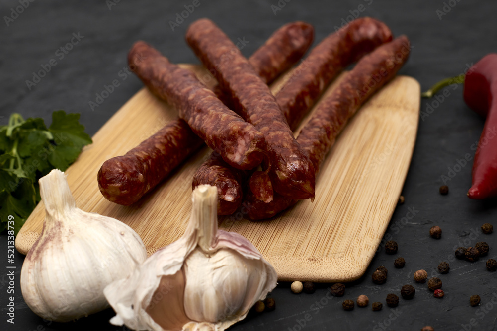 spicy smoked sausages on a cutting board next to red pepper garlic and herbs on a black background spicy smoked sausages on a cutting board next to red pepper garlic and herbs on a black background