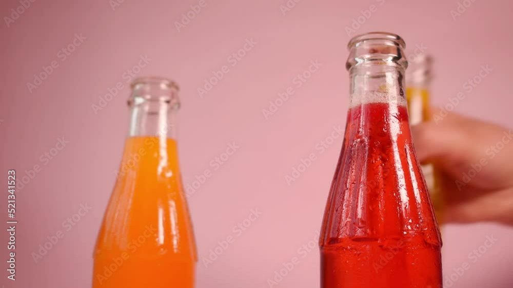 Closeup of a hand grabbing a bottle of lemonade or other refreshing juice on a pink background