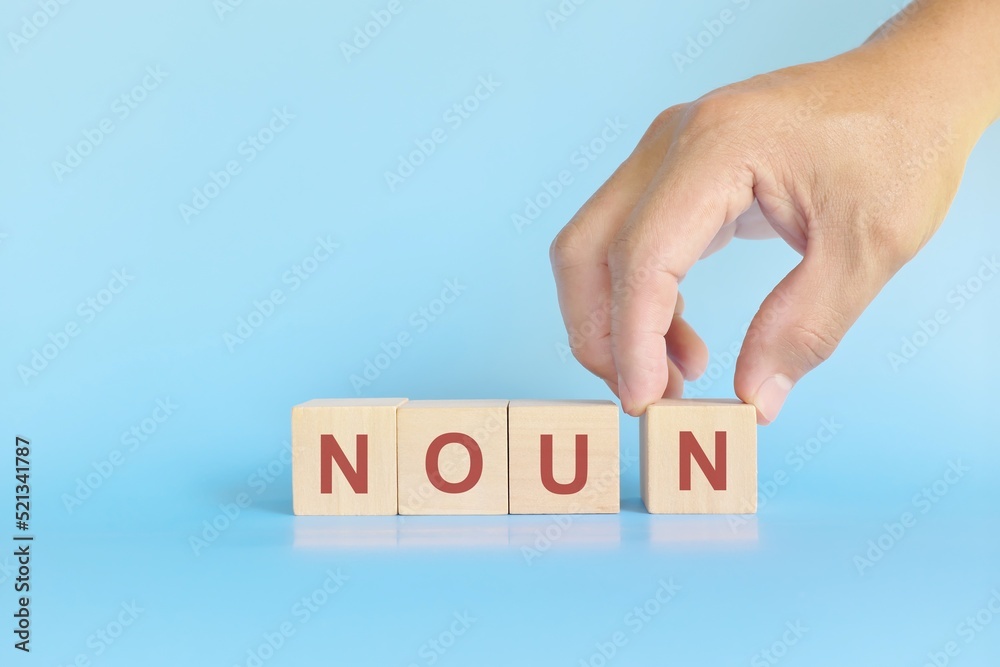 Noun concept in English grammar education. Wooden block crossword puzzle flat lay in blue background.