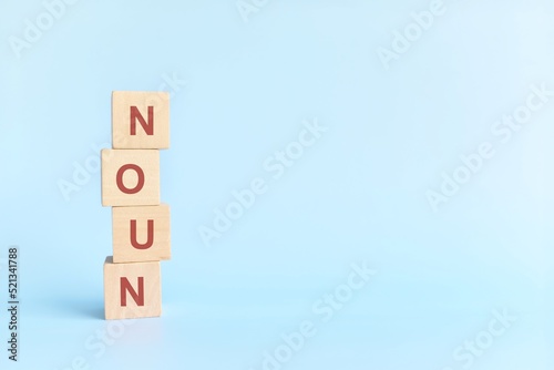 Noun concept in English grammar education. Wooden block crossword puzzle flat lay in blue background.