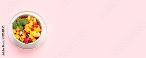 Bowl of tasty fruit salad on light pink background with space for text