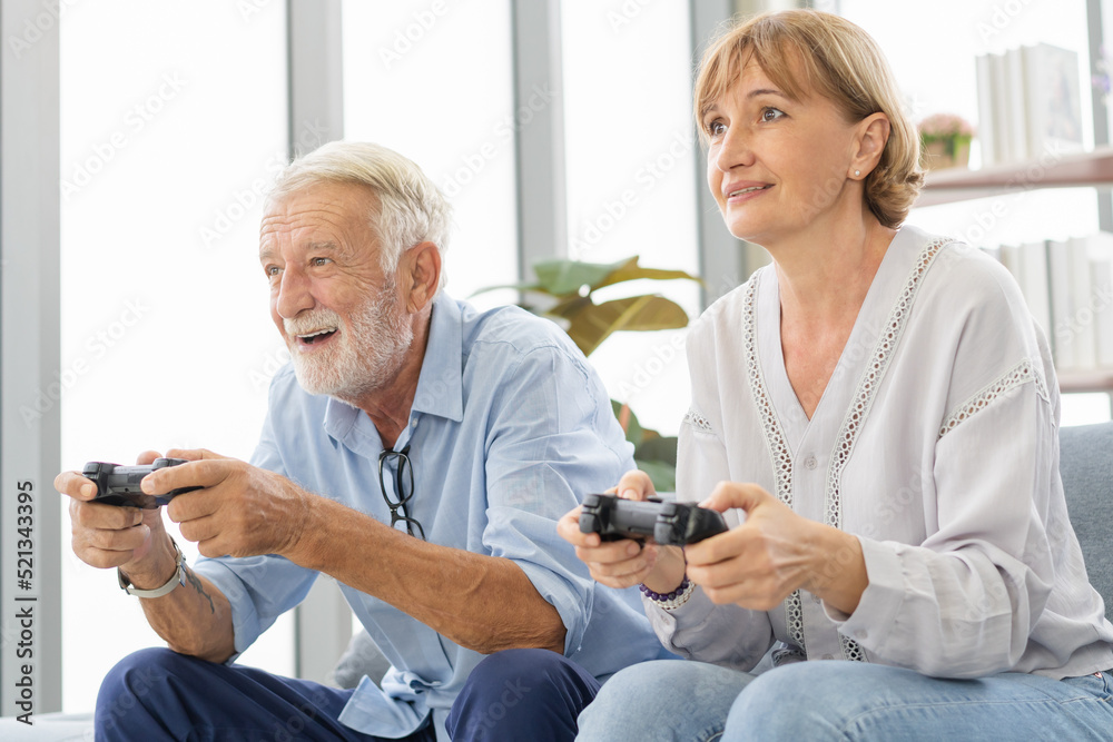 Obraz premium Happy senior couple, elderly family, Hand of caucasians mature, adult lover and retired husband, wife having fun, playing video game together, sitting cozy on sofa in living room at home, technology.