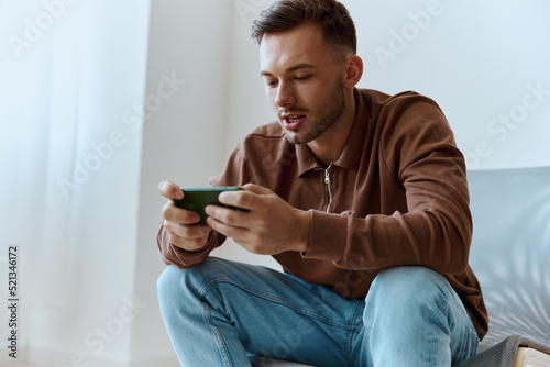 Enjoyed focused confused attractive try to win enthusiastically playing in exciting raising game looks at screen. Happy guy relaxing with phone chatting with friends. Mobile App concept. Copy space