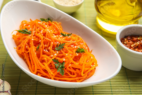 Bowl with delicious carrot salad on green bamboo mat, closeup