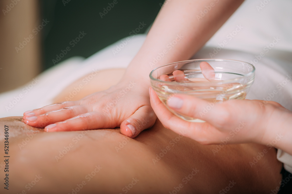 Massaging with massage oil, hands of a female massage therapist massaging a female client Massaging with massage oil, hands of a female massage therapist massaging a female client