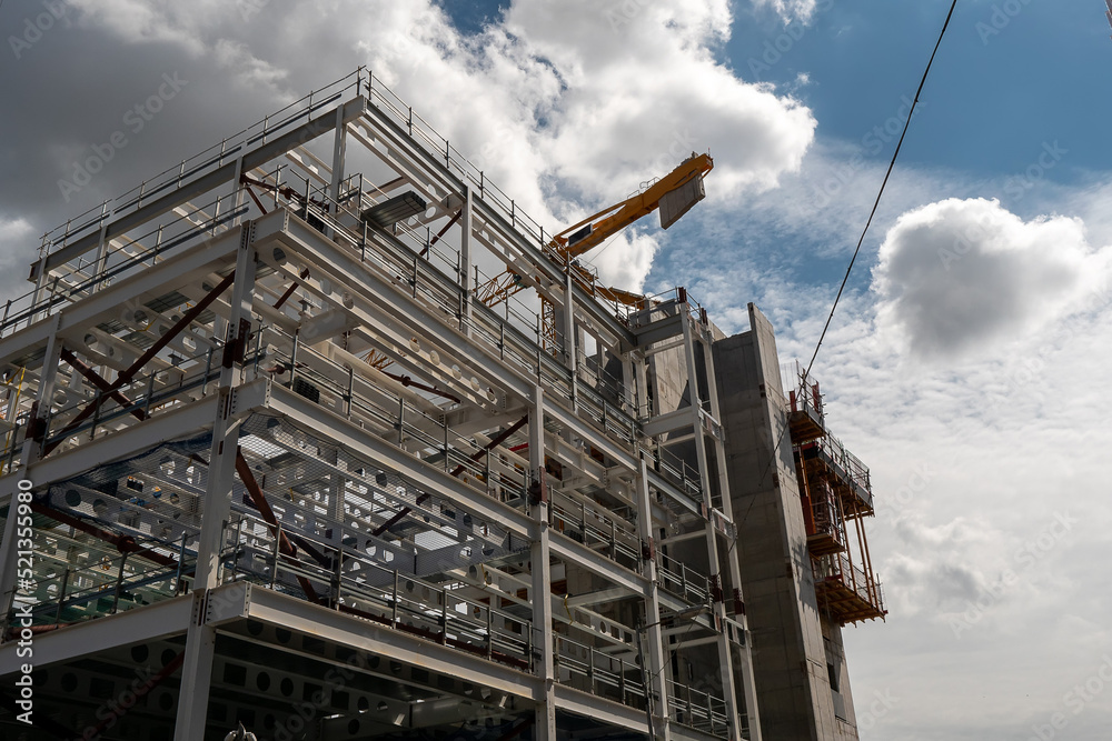 Construction of a modern tall building with metal frame. Developing residential and commercial high value property. Tall crane and cloudy sky in the background. Construction of a modern tall building with metal frame. Developing residential and commercial high value property. Tall crane and cloudy sky in the background.
