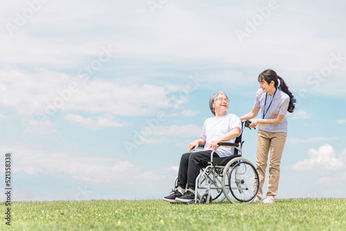 公園を散歩する介護士と車椅子の高齢者女性（青空）
 photo