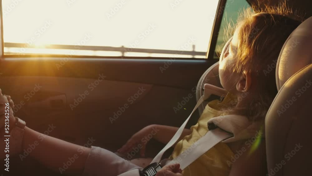The child sits in a child car seat while the car is moving and looks out the window. Travel concept.