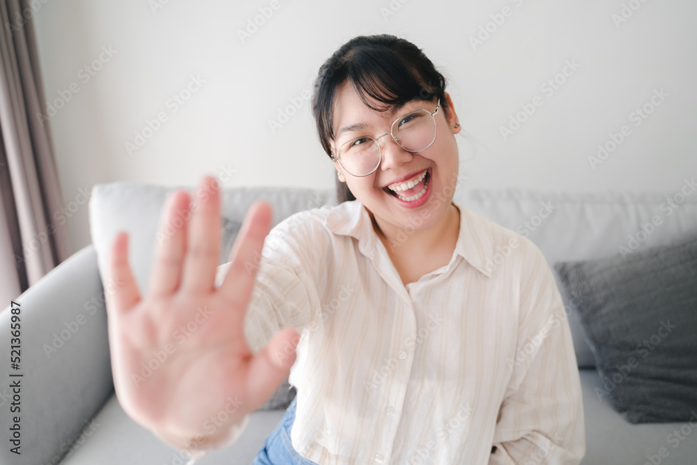 Young Asian woman using smartphone for online video conference call with friends waving hand making hello gesture