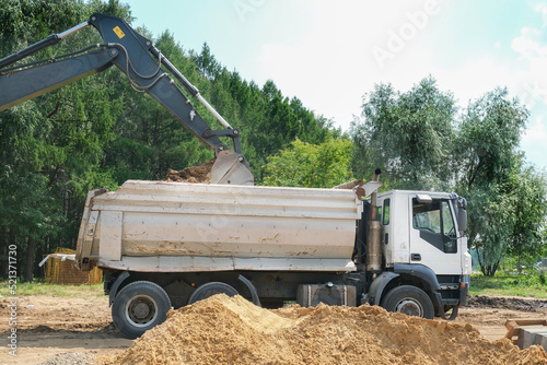 excavator with bucket loading sand into a truck at dirty construction site