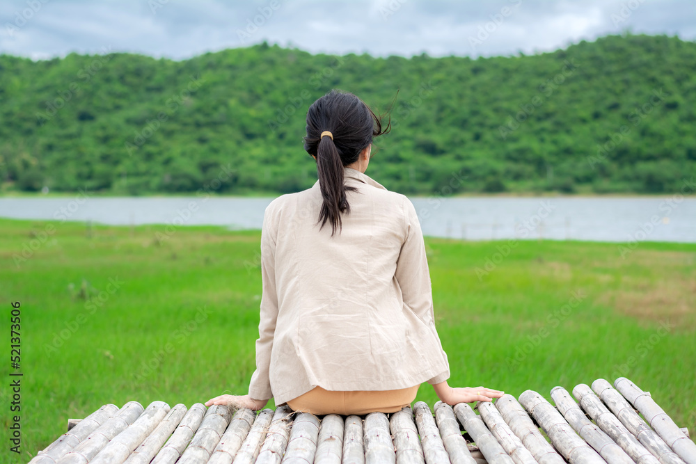 The young woman is sitting on the bamboo litter and looking at the view of the reservoir at the Huai Phak Reservoir, Tha Yang District, Phetchaburi, Thailand.