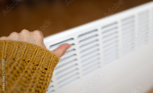 Woman warming her hand on a warm electric heater in a cold winter day at home. Saving electricity, heating season, energy crisis concept.