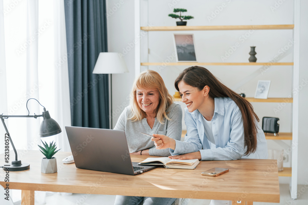 Learning how to use modern technologies. Smartphone and laptop. Mother and daughter is together at home Learning how to use modern technologies. Smartphone and laptop. Mother and daughter is together at home