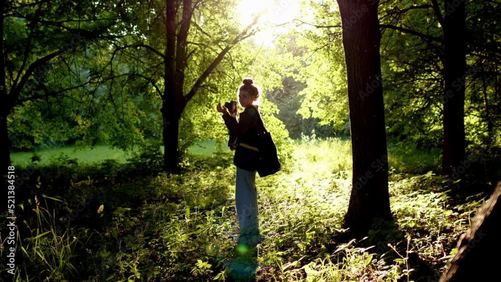 professional photographer chooses place for photo session in rays of setting sun, which creates excellent backlight on person. Woman in with camera stands in forest against backdrop of dawn sun professional photographer chooses place for photo session in rays of setting sun, which creates excellent backlight on person. Woman in with camera stands in forest against backdrop of dawn sun