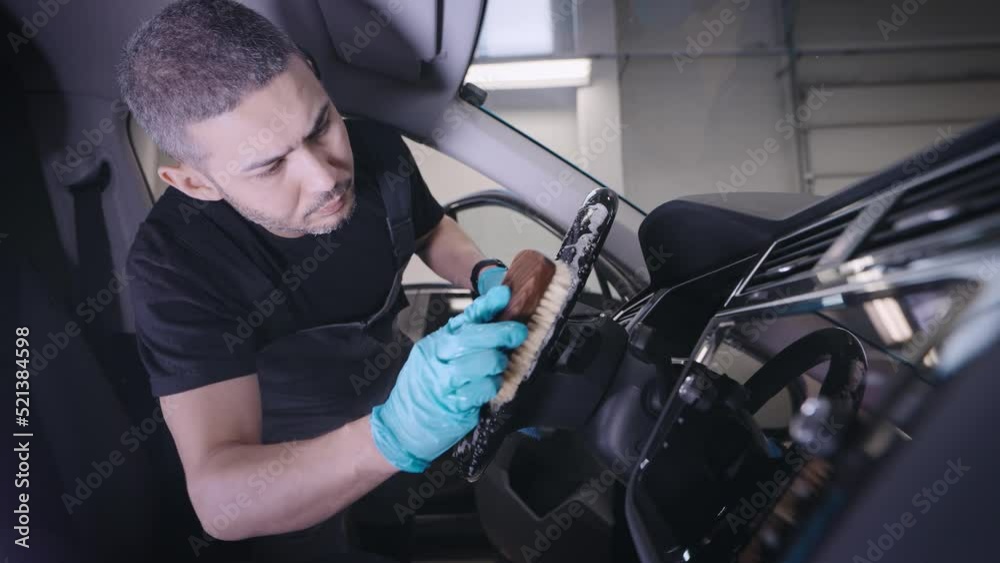 A man works in a detailing studio. A worker cleans the steering wheel of a car. A man works in a detailing studio. A worker cleans the steering wheel of a car.