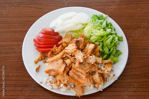 Turkish and Arabic Traditional Ramadan chicken doner kebab with tasty tomato sauce and rice or turkish pilav in white plate on wood table background. (Pilav ustu tavuk doner) photo