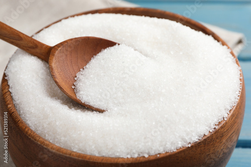 Granulated sugar and spoon in bowl on table, closeup