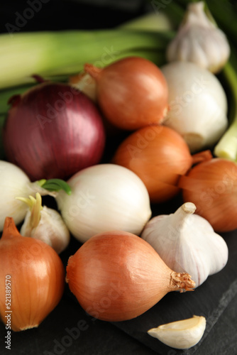 Fresh onion bulbs, leek and garlic on black table, closeup