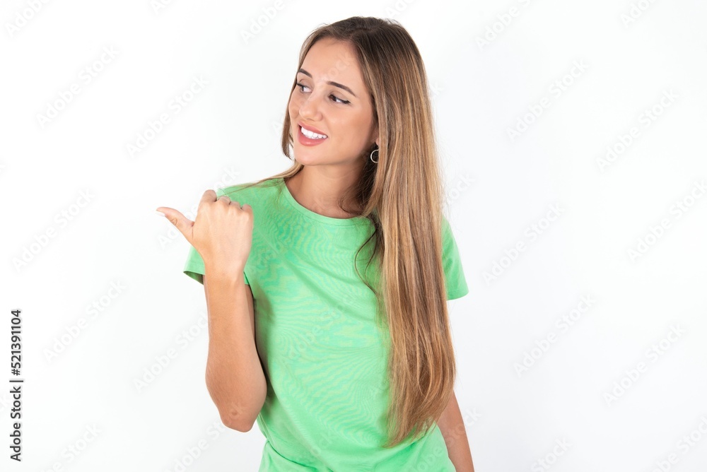 Charming young beautiful woman wearing green T-shirt over white background looking at copy space having advertisements Charming young beautiful woman wearing green T-shirt over white background looking at copy space having advertisements
