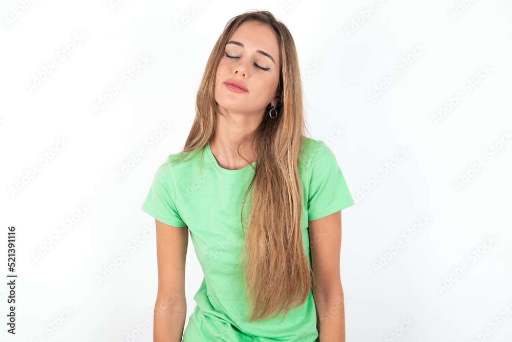 young beautiful woman wearing green T-shirt over white background looking sleepy and tired, exhausted for fatigue and hangover, lazy eyes in the morning. young beautiful woman wearing green T-shirt over white background looking sleepy and tired, exhausted for fatigue and hangover, lazy eyes in the morning.