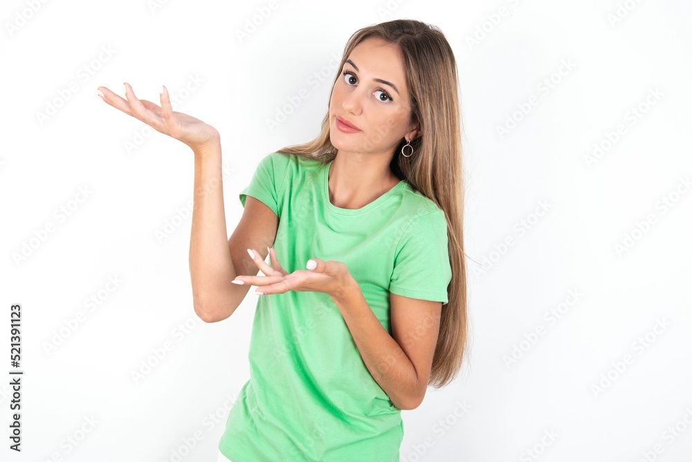 young beautiful woman wearing green T-shirt over white background pointing aside with both hands showing something strange and saying: I don't know what is this. Advertisement concept. young beautiful woman wearing green T-shirt over white background pointing aside with both hands showing something strange and saying: I don't know what is this. Advertisement concept.