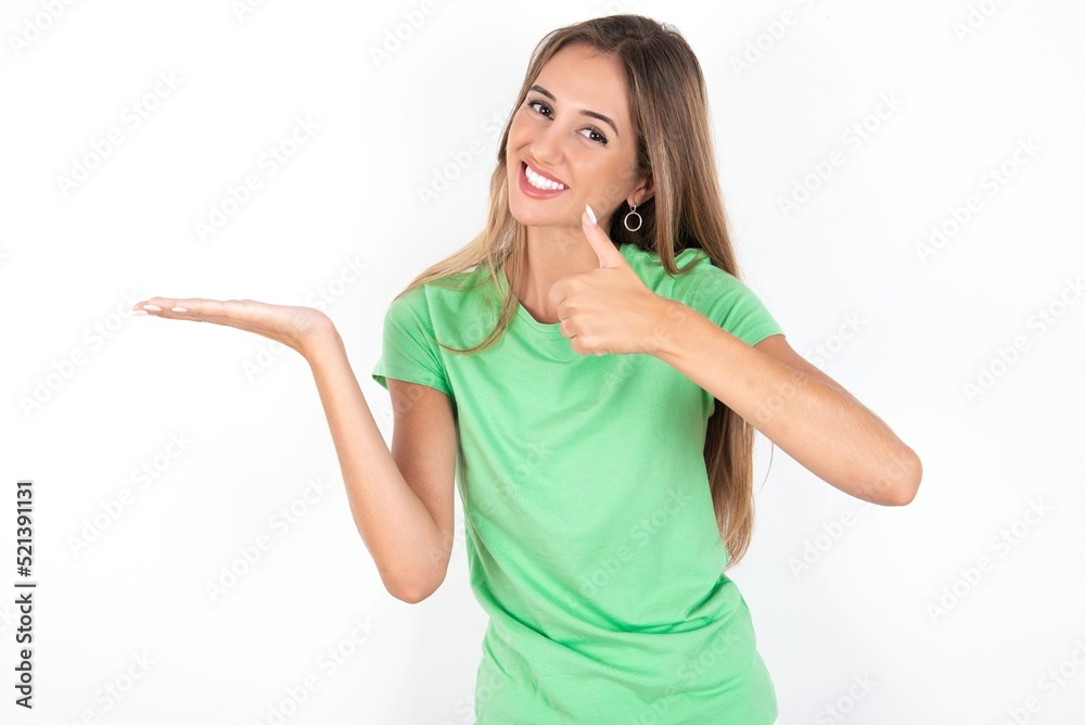 young beautiful woman wearing green T-shirt over white background Showing palm hand and doing ok gesture with thumbs up, smiling happy and cheerful. young beautiful woman wearing green T-shirt over white background Showing palm hand and doing ok gesture with thumbs up, smiling happy and cheerful.
