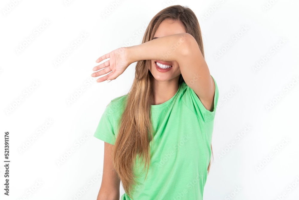 young beautiful woman wearing green T-shirt over white background covering eyes with arm smiling cheerful and funny. Blind concept. young beautiful woman wearing green T-shirt over white background covering eyes with arm smiling cheerful and funny. Blind concept.