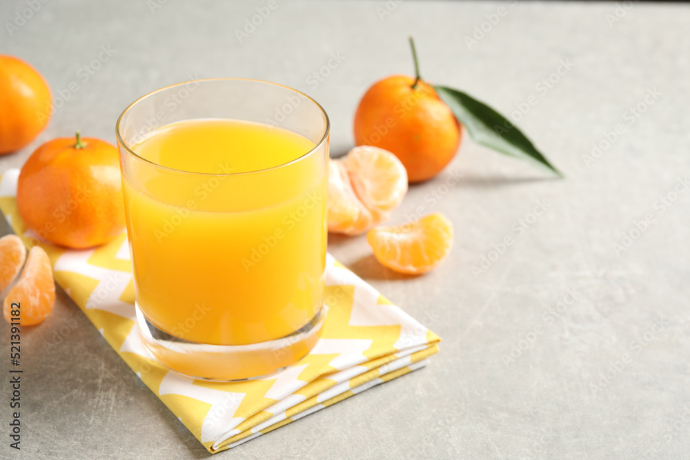 Fototapeta premium Glass of fresh tangerine juice and fruits on light grey table. Space for text