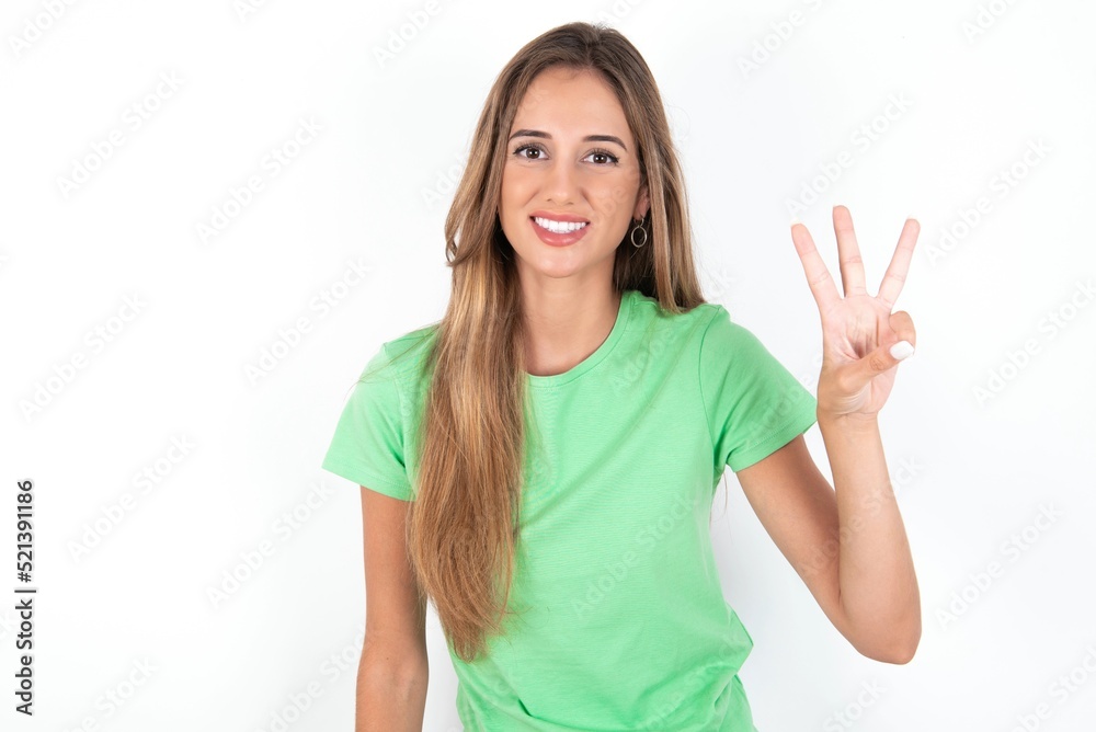 young beautiful woman wearing green T-shirt over white background showing and pointing up with fingers number three while smiling confident and happy. young beautiful woman wearing green T-shirt over white background showing and pointing up with fingers number three while smiling confident and happy.