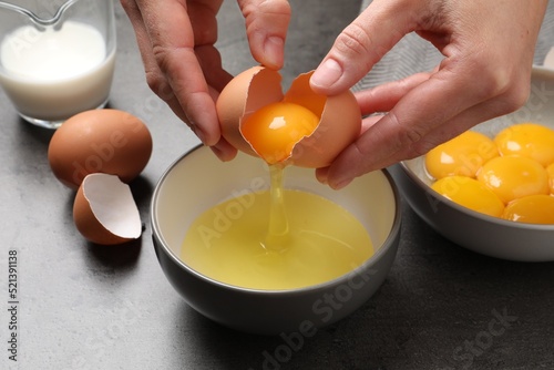 Woman separating egg yolk from white over bowl at grey table, closeup photo