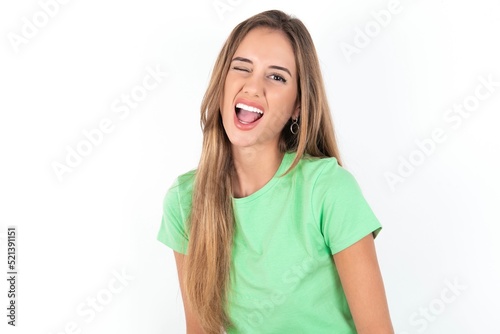 young beautiful woman wearing green T-shirt over white background winking looking at the camera with sexy expression, cheerful and happy face.