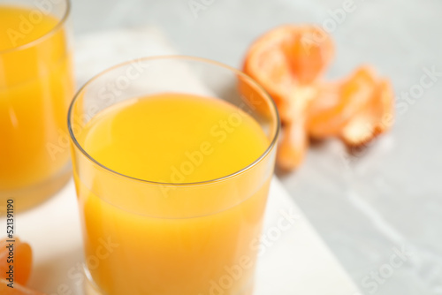 Glass of fresh tangerine juice and fruits on table, closeup